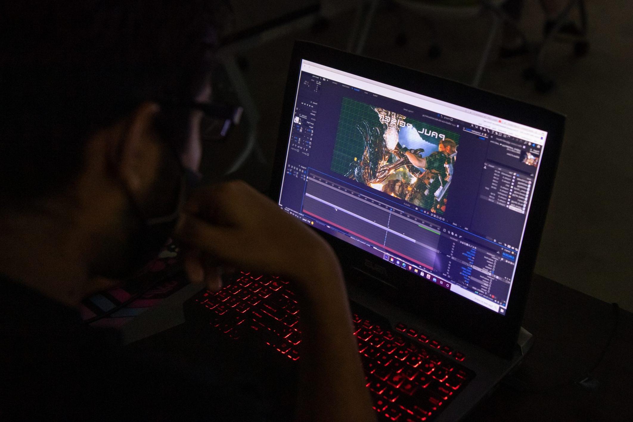 Student sitting in the dark on a laptop working on 动画 assignment