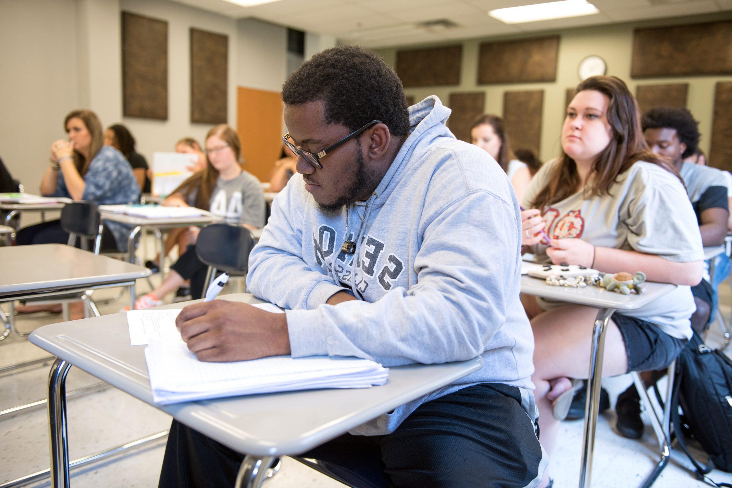 Student in class sitting at a desk, writing in tablet.